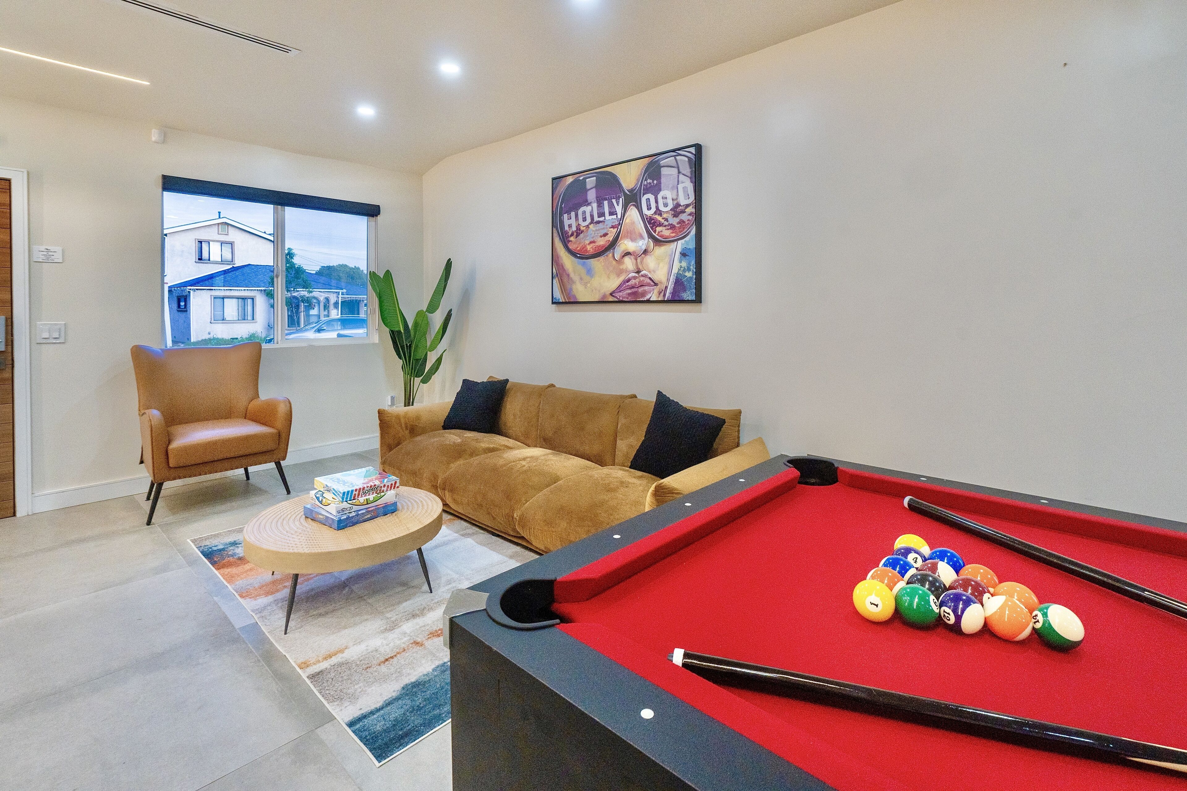 Een pooltafel met ballen, een bank, een stoel en een raam met uitzicht op huizen.