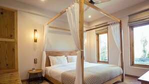 Una cama con dosel y cuatro columnas, un cabecero de madera y una mesita de noche con una lámpara.