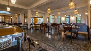 Un comedor amplio con varias mesas y sillas, ventanas grandes y lámparas colgantes.