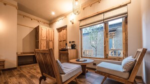 Una habitación acogedora con muebles de madera, una mesita y una ventana con vistas a un edificio y un árbol.