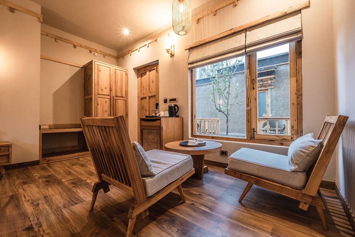 A cozy room with wooden furniture, a small table, and a window with a view of a building and a tree.