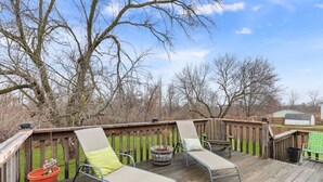 Eine Holzterrasse mit zwei Liegestühlen, einem Topfpflanzen und einem Gartenhaus im Hintergrund.