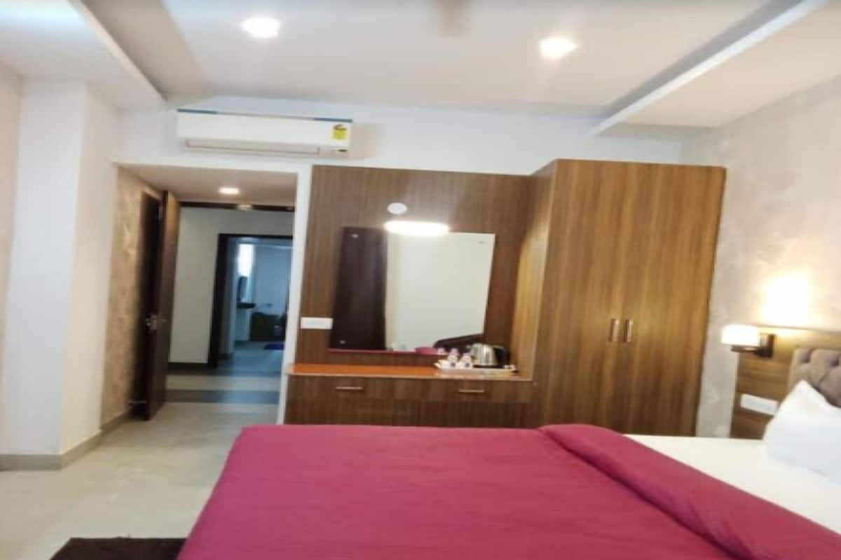 Une chambre d’hôtel avec un lit, une armoire en bois, un miroir et un bureau avec une lampe.