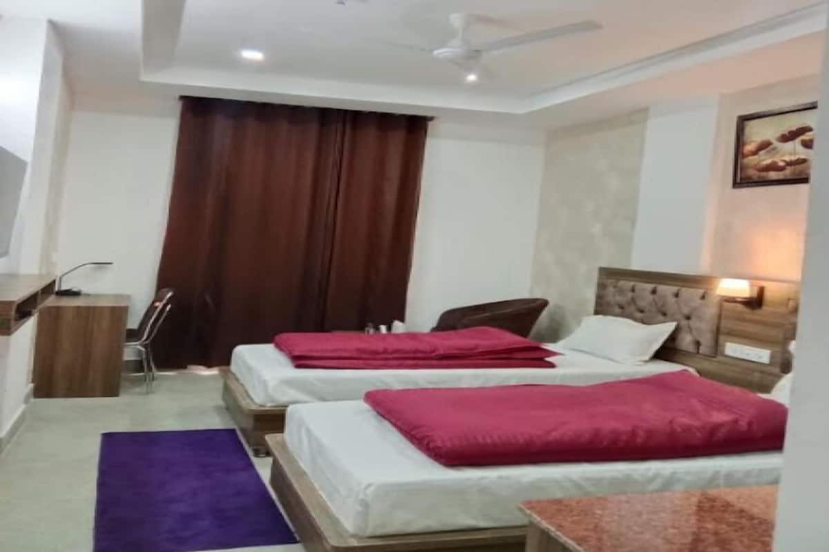 Une chambre d’hôtel avec deux lits, un bureau, une chaise, un tapis violet et un ventilateur de plafond.
