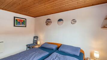 Een slaapkamer met twee bedden, een houten plafond, een wandradiator, een stoel en een ingelijst kunstwerk.