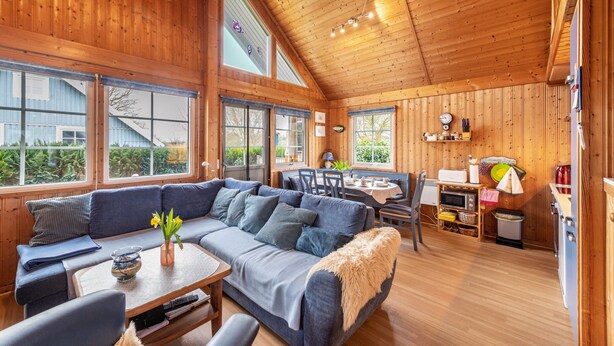 Una cabaña acogedora con interior de madera, un sofá, una mesa de comedor y una zona de cocina.