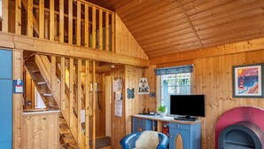Interior de una cabaña de madera con escalera, televisor, chimenea y escritorio con computadora.