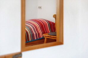 A room with a bed, a chair, and a mirror reflecting the bed.