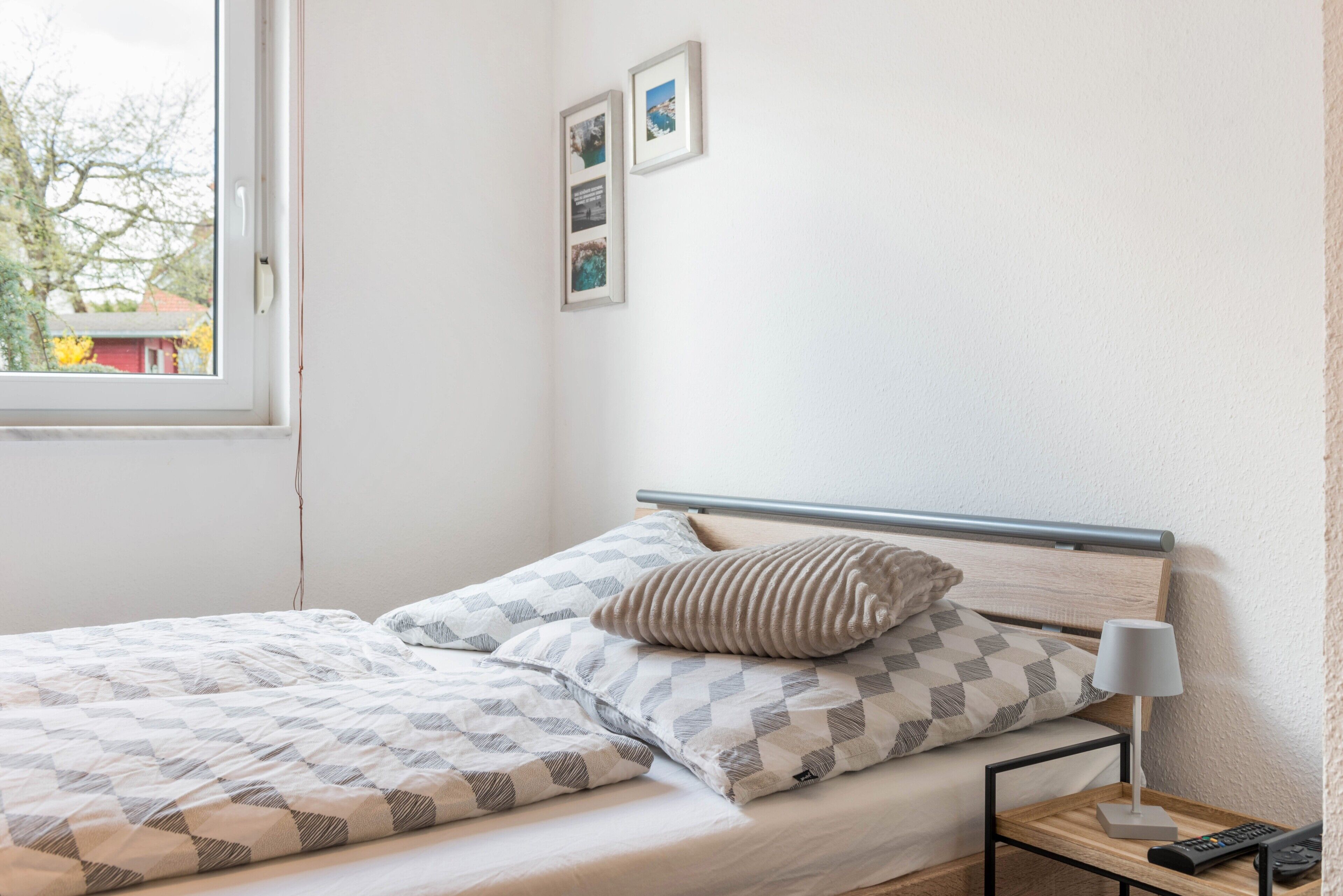 Un lit bien fait, recouvert d’une couvre-lit à motifs, avec un oreiller, une table de chevet dotée d’une lampe et deux tableaux encadrés accrochés au mur.