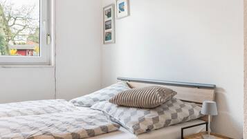 Un lit bien fait, recouvert d’une couvre-lit à motifs, avec un oreiller, une table de chevet dotée d’une lampe et deux tableaux encadrés accrochés au mur.