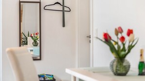 Una habitación con espejo, perchero, mesa con un jarrón de flores y una silla.