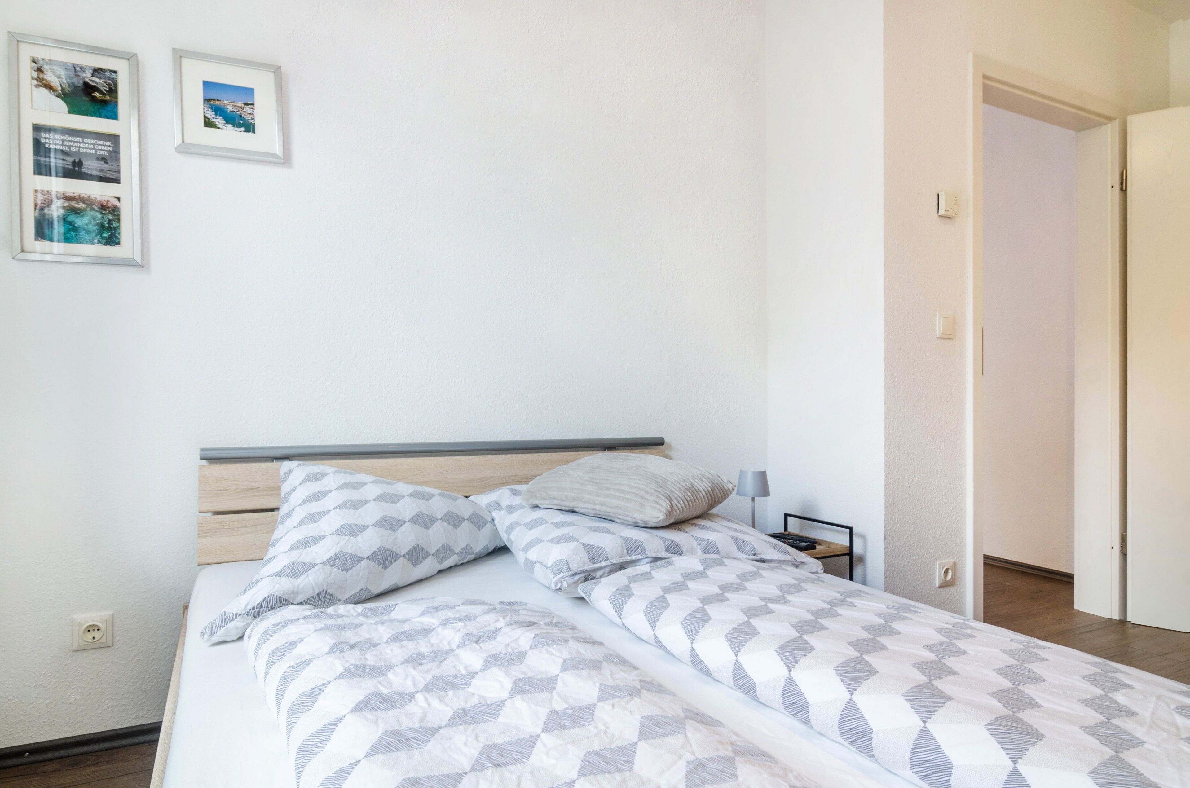 Een bed met beddengoed met patroon, een nachtkastje met een lamp, en twee ingelijste foto's aan de muur.