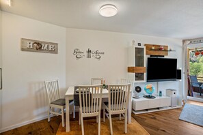 Ein Essbereich mit einem weißen Tisch, Stühlen und einem an der Wand befestigten Fernseher.