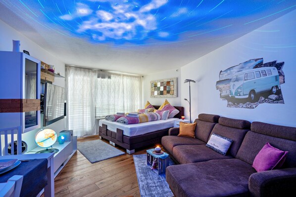 Ein modernes Schlafzimmer mit einem Bett, einer Couch, einem Schreibtisch und einer Decke mit Lichteffekten.