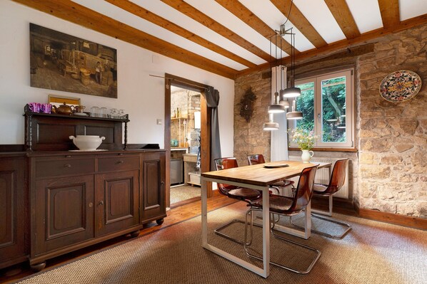 Une cuisine rustique avec des poutres en bois, un mur en pierre et un coin repas comprenant une table et des chaises.