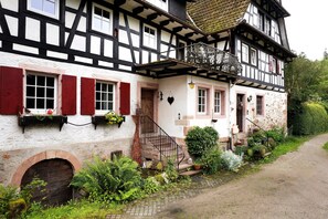 Un bâtiment traditionnel à colombages, doté d’une façade en pierre, d’une porte en bois et d’un escalier menant à l’entrée.