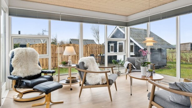 A spacious sunroom with large windows, a wooden ceiling, and a variety of seating options including a black leather chair, a wooden sofa, and a cushioned bench. - "Fentje" - 200m from the sea by Interhome (Frørup)
