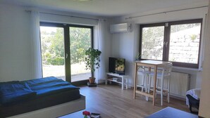 Une chambre avec un lit, une télévision, une petite table avec une plante et une fenêtre donnant sur des arbres.