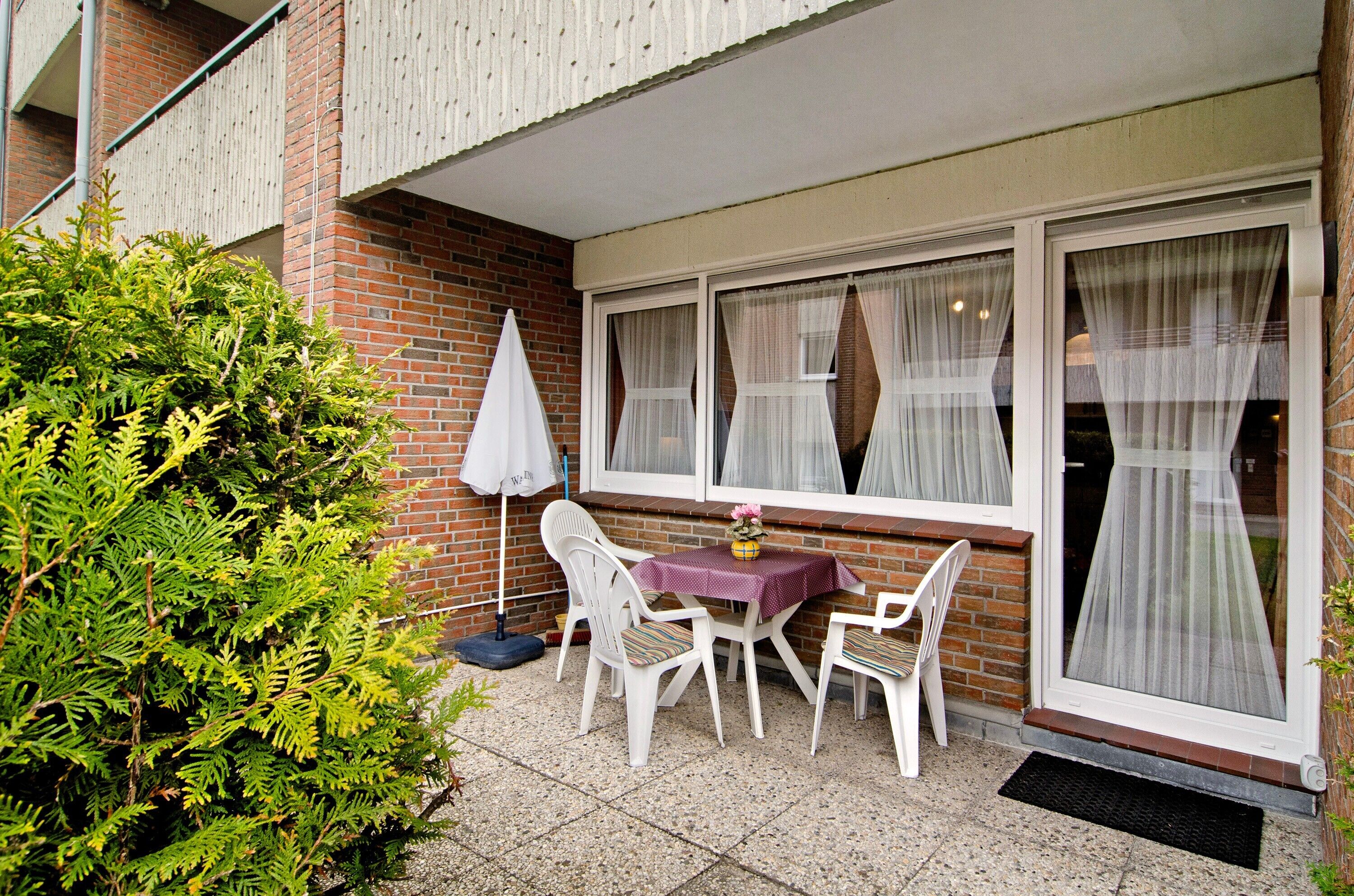 Eine Terrasse im Freien mit Tisch und Stühlen, einem Blumentopf und einem Fenster mit Vorhängen.