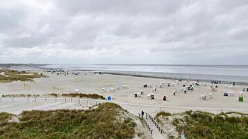 Ein Strand mit einem Sandweg zum Wasser, einer Reihe von Strandkörben und einem bewölkten Himmel.