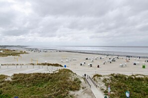 Ein Strand mit einem Sandweg zum Wasser, einer Reihe von Strandkörben und einem bewölkten Himmel.