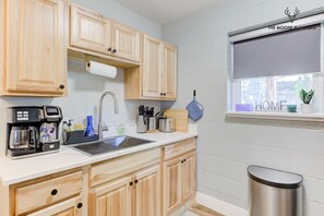 A kitchen with wooden cabinets, a coffee maker, a sink, and a window with a view of the outside.