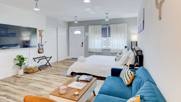 A modern hotel room with a bed, a blue sofa, a coffee table, a guitar, and a TV. - Luxe Modern loft w/ King Bed, Free Parking & Wi-Fi (Memphis)