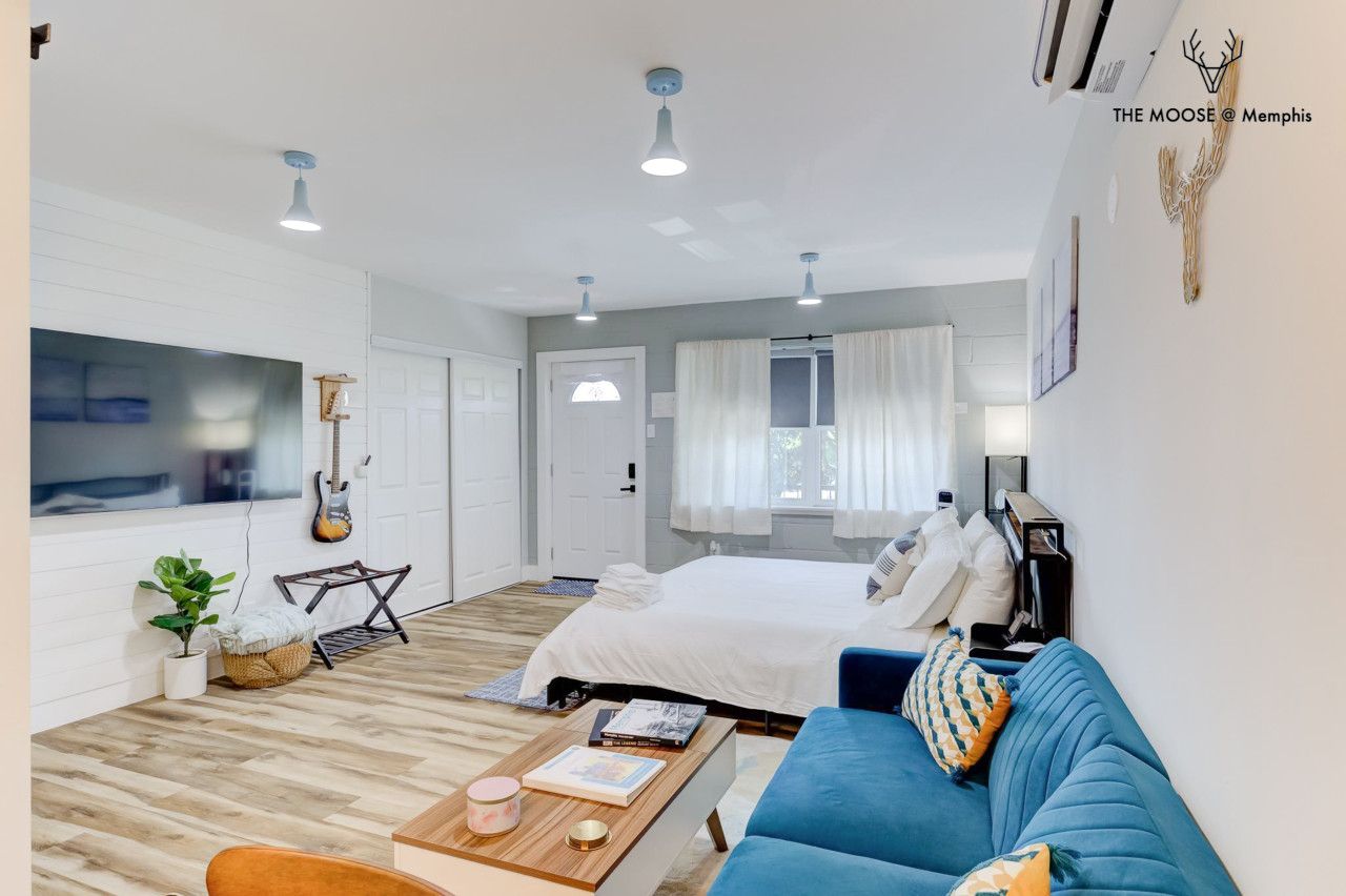 A modern hotel room with a bed, a blue sofa, a coffee table, and a guitar on the wall.