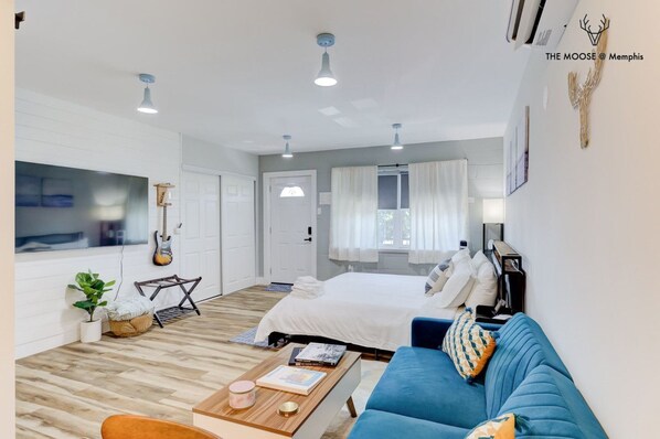 A modern hotel room with a bed, a blue sofa, a coffee table, and a guitar on the wall.