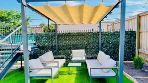 A covered patio with white outdoor furniture, a pergola, and a neatly trimmed hedge. - Luxe Modern loft w/ King Bed, Free Parking & Wi-Fi (Memphis)