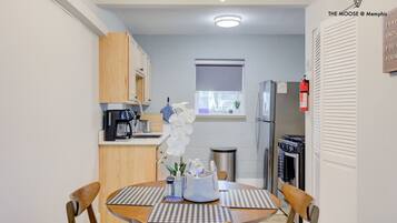 A compact kitchen with a dining area, a refrigerator, a coffee machine, and a window with a view.