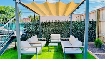 Eine überdachte Terrasse mit weißer Gartenmöbeln, einem Pergola und einer ordentlich geschnittenen Hecke.
