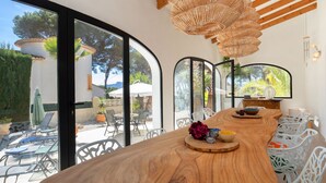 A modern kitchen with a large wooden island, white chairs, and a view of the outdoor patio. - Vacation home Angela by Interhome (Benissa)