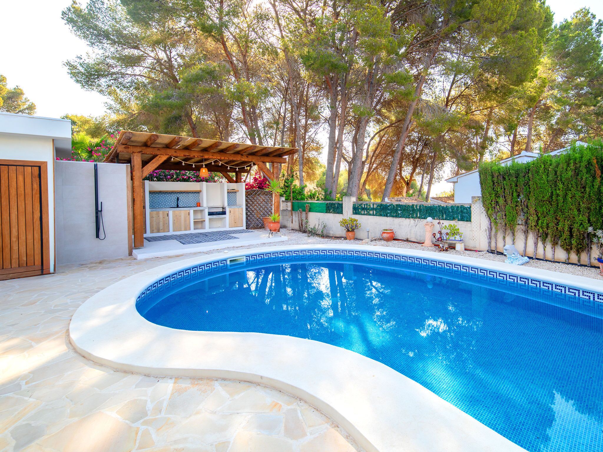 Une piscine entourée d’une terrasse en pierre, agrémentée d’une pergola en bois et de plantes en pot.