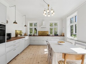 Una cocina moderna con armarios blancos, encimera de madera, una mesa de comedor con sillas y una araña.