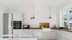 Une cuisine moderne avec des meubles blancs, un plan de travail en bois, un four encastré, un four à micro-ondes et un coin repas avec une table et des chaises.