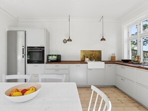 A modern kitchen with white cabinetry, a wooden countertop, a built-in oven, a microwave, and a dining area with a table and chairs.