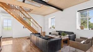 Un vaste espace de vie agrémenté d’un escalier en bois, d’un canapé, d’une table basse et offrant une vue sur l’extérieur.
