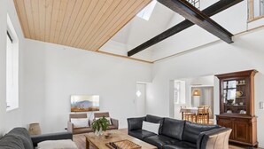 Un vaste salon doté d’un haut plafond, d’une cheminée et d’un coin repas visible à travers une porte ouverte.