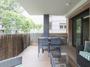 Un balcon avec une table et des chaises, un canapé en osier et une cloison en verre.