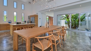 A spacious kitchen with a long wooden table and chairs, a built-in oven, and a large window with a view of greenery.