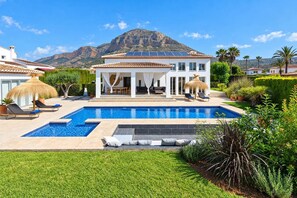 Een tweelaags huis met een zwembad, een overdekt terras en een berg op de achtergrond.