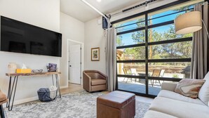 A modern living room with a large TV, a sofa, a chair, and a small table.