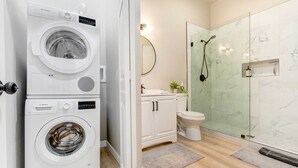 A modern bathroom with a Bosch washing machine, a toilet, a glass shower enclosure, and a marble-tiled wall.
