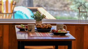 A wooden table with a plate of fruit, a bowl of cookies, and two mugs with a deer design. - Riverfront Fire Pit, Gas Stove, Near Skiing, Hot Springs, & Hiking Adventures! (Pagosa Springs)