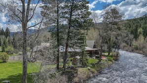 A riverside property with a cabin, a grassy area, and a forested backdrop. - Riverfront Fire Pit, Gas Stove, Near Skiing, Hot Springs, & Hiking Adventures! (Pagosa Springs)
