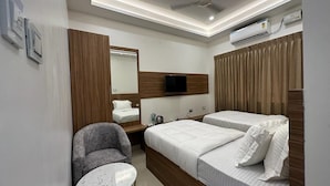 Una habitación de hotel con cama, una silla, una mesita, ventilador de techo y aire acondicionado.