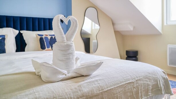 Hotellihuone, jossa on sänky, sydämenmuotoinen pyyheasetelma, peili ja sininen seinä.