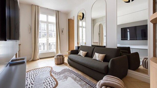 A modern living room with a sofa, a TV, and a large window.
