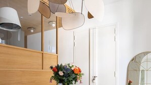 A modern dining area with a round wooden table, two teal upholstered chairs with gold legs, and a vase of flowers.